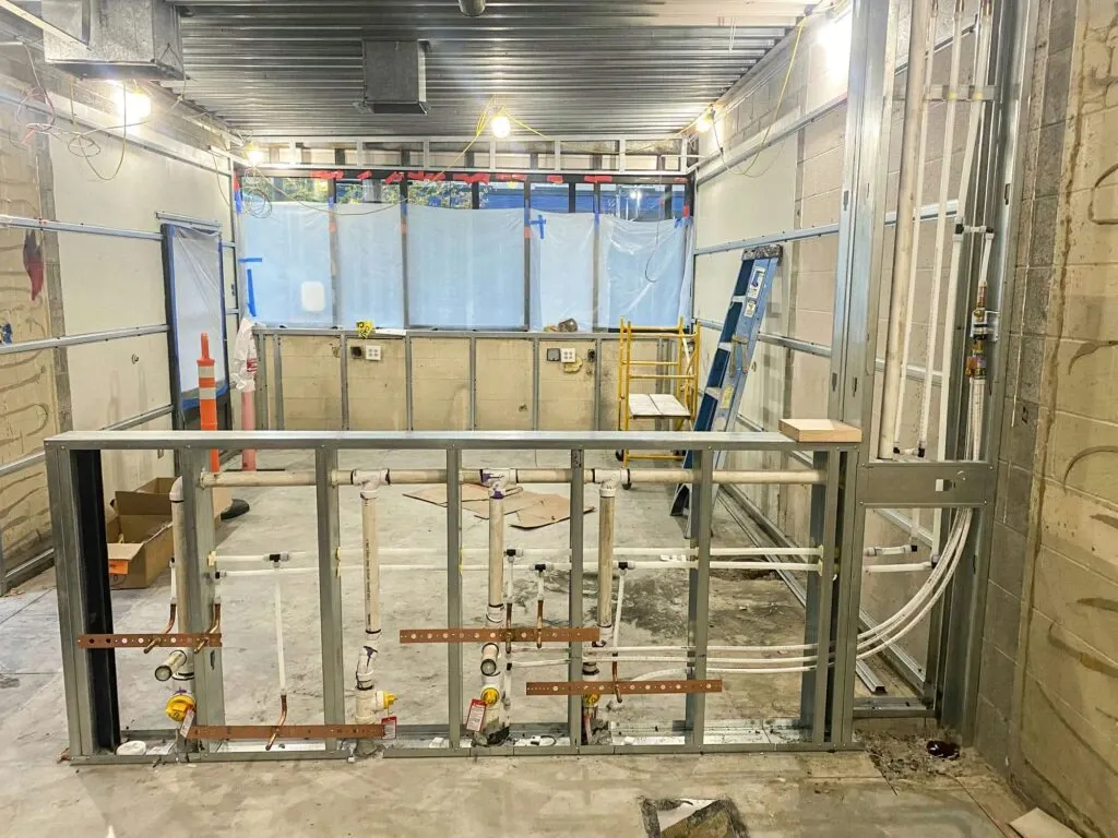 Professional commercial plumbing rough-in for a restaurant kitchen expansion, featuring code-compliant copper and PVC lines in metal stud framing